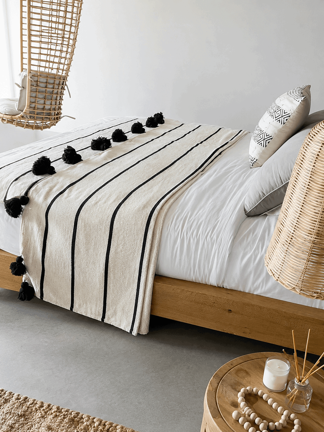 Couverture marocaine noire et blanche à pompons sur un lit avec décoration naturelle